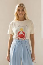 Βαμβακερό Κοντομάνικο T-Shirt “La Dolce Vita” Το βαμβακερό κοντομάνικο T-shirt “La Dolce Vita” είναι η ιδανική επιλογή για casual και καλοκαιρινά looks με ιταλικό αέρα. Διαθέτει εντυπωσιακή στάμπα με crab print και lettering, που δίνει playful και fresh χαρακτήρα στο outfit. Η γραμμή του είναι άνετη και χαλαρή, καλύπτοντας έως Large, ενώ το μαλακό βαμβακερό ύφασμα με ελαστικότητα προσφέρει άνεση και ευχάριστη αίσθηση όλη την ημέρα. Ιδανικό για καθημερινές εμφανίσεις, ταξίδια και city looks. Styling Tip Συνδύασέ το με ψηλόμεση παντελόνα ή denim shorts για relaxed καλοκαιρινό look. Με λινή παντελόνα και sneakers αποκτά πιο chic casual χαρακτήρα, ενώ με σακάκι γίνεται ιδανικό για smart everyday εμφανίσεις.