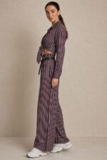Ριγέ satin-effect Σετ  purple Χαρακτηριστικά Πουκάμισο 100% Viscose με satin-effect επεξεργασία Κλασικός γιακάς Κουμπιά μπροστά Μακρύ μανίκι Κανονικό μήκος Κανονική προς άνετη γραμμή Μπορεί να δεθεί μπροστά Πολύ απαλή & δροσερή αίσθηση Παντελόνα 100% Viscose με satin-effect επεξεργασία Wide-leg γραμμή Λάστιχο στη μέση μπροστά και πίσω Πλαϊνές τσέπες Άνετη, ρευστή εφαρμογή Διαστάσεις Πουκάμισο Στήθος: έως 112 cm Περιφέρεια: έως 116 cm Μήκος: 66 cm Παντελόνα Μέση: ελαστική, έως 96 cm Περιφέρεια: έως 116 cm Μήκος: 108 cm Φροντίδα Πλύσιμο σε κρύο νερό Χωρίς στύψιμο Χαμηλές στροφές Όχι στεγνωτήριο Στέγνωμα φυσικά, χωρίς άμεση έκθεση στον ήλιο Non-iron – δεν απαιτεί σιδέρωμα Αίσθηση υφάσματος Το ύφασμα είναι εξαιρετικά μαλακό, ελαφρύ και δροσερό στην επαφή με το σώμα, χωρίς τραχιά αίσθηση. Η απαλή viscose το καθιστά μια ιδιαίτερα άνετη επιλογή και για ευαίσθητες επιδερμίδες. Σε περίπτωση γνωστής αλλεργίας ή ιδιαίτερης δερματικής ευαισθησίας, συνιστάται πάντα να λαμβάνεται υπόψη η ατομική αντίδραση στα υφάσματα.