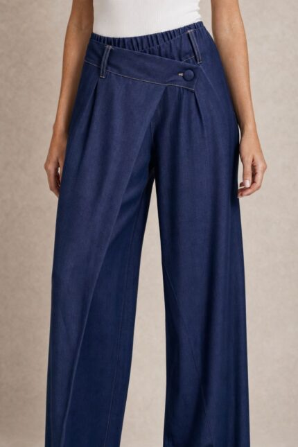 Viscose Denim Wrap Wide Leg Pants Χαρακτηριστικά Ύφασμα: Viscose με denim effect Υφή: Πολύ μαλακή και απαλή Αίσθηση: Ελαστική και άνετη Γραμμή: Wide leg Μέση: Ιδιαίτερη λοξή / asymmetric wrap μέση Λάστιχο στη μέση για μεγαλύτερη άνεση Λεπτομέρεια: Διακοσμητικό κουμπί στο μπροστινό μέρος Τσέπες: Πλαϊνές Εφαρμογή: Άνετη, με ρευστό πέσιμο Μέγεθος: One Size Καλύπτει έως Large Sensitive Skin Friendly Η απαλή viscose και η μαλακή αίσθηση του υφάσματος την καθιστούν κατάλληλη επιλογή για όσους προτιμούν μαλακά υφάσματα ή έχουν ευαίσθητο δέρμα. Σε αντίθεση με ένα πιο άκαμπτο denim, έχει πιο ήπια και ευχάριστη επαφή με το σώμα. Φροντίδα Πλύσιμο έως 30°C, σε χαμηλές στροφές. Αποφύγετε το έντονο στύψιμο. Εάν χρειαστεί σιδέρωμα, χρησιμοποιήστε χαμηλή θερμοκρασία. Προτείνεται φυσικό στέγνωμα και αποφυγή πολύωρης άμεσης έκθεσης στον ήλιο, ώστε να διατηρηθεί καλύτερα η απόχρωση και η υφή του υφάσματος.