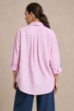 Cotton Oversized Heart Shirt  Χαρακτηριστικά Προϊόντος Ύφασμα: Μαλακό, σταθερό βαμβακερό ύφασμα Γραμμή: Oversized / Relaxed Fit Μέγεθος: One Size – καλύπτει έως Large Plus Ροζ βάση με λεπτές λευκές κάθετες ρίγες Κόκκινη κεντητή καρδιά στο μπροστινό μέρος Κλασικός γιακάς πουκαμίσου Κλείσιμο μπροστά με κουμπιά Μακριά μανίκια με μανσέτες Χαμηλή ραφή ώμων (dropped shoulders) Ασύμμετρο μήκος, πιο μακρύ πίσω Στρογγυλεμένο τελείωμα Πιέτα στην πλάτη για μεγαλύτερη άνεση Φαρδιά, αέρινη εφαρμογή Μέτρηση One Size Στήθος έως 125 cm Περιφέρεια έως 130 cm Οδηγίες Φροντίδας Πλύσιμο έως 30°C Χωρίς στύψιμο Πλύσιμο με παρόμοια χρώματα Προτείνεται πλύσιμο από την ανάποδη για προστασία του κεντήματος Φυσικό στέγνωμα σε σκιερό μέρος Όχι στεγνωτήριο Σιδέρωμα σε χαμηλή προς μέτρια θερμοκρασία, σύμφωνα με την ετικέτα σύνθεσης Αποφύγετε το απευθείας σιδέρωμα πάνω στην κεντητή καρδιά