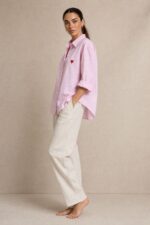 Cotton Oversized Heart Shirt  Χαρακτηριστικά Προϊόντος Ύφασμα: Μαλακό, σταθερό βαμβακερό ύφασμα Γραμμή: Oversized / Relaxed Fit Μέγεθος: One Size – καλύπτει έως Large Plus Ροζ βάση με λεπτές λευκές κάθετες ρίγες Κόκκινη κεντητή καρδιά στο μπροστινό μέρος Κλασικός γιακάς πουκαμίσου Κλείσιμο μπροστά με κουμπιά Μακριά μανίκια με μανσέτες Χαμηλή ραφή ώμων (dropped shoulders) Ασύμμετρο μήκος, πιο μακρύ πίσω Στρογγυλεμένο τελείωμα Πιέτα στην πλάτη για μεγαλύτερη άνεση Φαρδιά, αέρινη εφαρμογή Μέτρηση One Size Στήθος έως 125 cm Περιφέρεια έως 130 cm Οδηγίες Φροντίδας Πλύσιμο έως 30°C Χωρίς στύψιμο Πλύσιμο με παρόμοια χρώματα Προτείνεται πλύσιμο από την ανάποδη για προστασία του κεντήματος Φυσικό στέγνωμα σε σκιερό μέρος Όχι στεγνωτήριο Σιδέρωμα σε χαμηλή προς μέτρια θερμοκρασία, σύμφωνα με την ετικέτα σύνθεσης Αποφύγετε το απευθείας σιδέρωμα πάνω στην κεντητή καρδιά