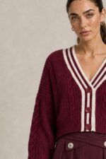 GNT Cable Knit Cardigan in Burgundy Χαρακτηριστικά Προϊόντος • Ύφασμα: Μαλακό πλεκτό • Ανάγλυφη cable knit / πλεξούδα ύφανση • V λαιμόκοψη • Contrast πλεκτή λεπτομέρεια περιμετρικά • Κλείσιμο μπροστά με κουμπιά • Μακριά μανίκια • Rib τελείωμα σε μανίκια και κάτω μέρος • Κανονική γραμμή • Κανονικό προς ελαφρώς cropped μήκος • Μαλακή και άνετη αίσθηση • One Size – καλύπτει έως Large Οδηγίες Φροντίδας • Πλύσιμο σε κρύο νερό • Στύψιμο μόνο σε χαμηλές στροφές • Στέγνωμα οριζόντια πάνω στην απλώστρα, ώστε να διατηρεί τη φόρμα του πλεκτού • Αποφύγετε το στεγνωτήριο και την άμεση επαφή με πηγές θερμότητας